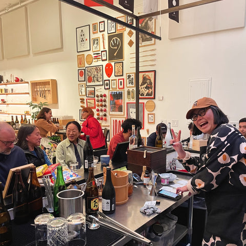 A group of people gathered around a bar counter, with bottles and glasses, enjoying drinks and conversation.